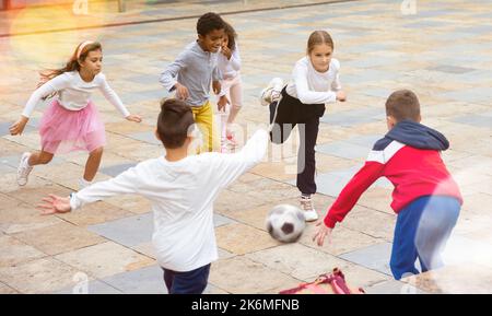 Eine Gruppe von Tweenagern, die nach dem Unterricht im Schulhof Fußball spielen Stockfoto