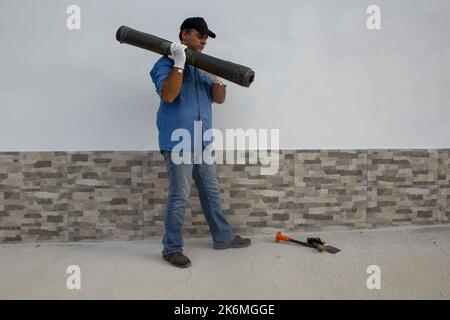 Bauarbeiter, der eine Rolle bituminöser Klebstoffummantelung auf seiner Schulter trägt, um Dächer und Böden zu isolieren. Bauarbeiten und Schutz Stockfoto