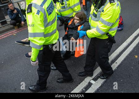 London, Großbritannien. 14.. Oktober 2022. Metropolitan Police Officers verhaften einen Klimaaktivisten von Just Stop Oil, der die Straße vor New Scotland Yard blockiert hatte, um die britische Regierung aufzufordern, die Erteilung von Öl- und Gaslizenzen einzustellen. Ein Aktivist besprühte auch das rotierende Schild von New Scotland Yard vor dem Gebäude mit gelber Farbe. Die Metropolitan Police nahm 24 Verhaftungen wegen des Verdachts der vorsätzlichen Behinderung der Autobahn und/oder der Verschwörung zur Begehung krimineller Schäden vor. Kredit: Mark Kerrison/Alamy Live Nachrichten Stockfoto