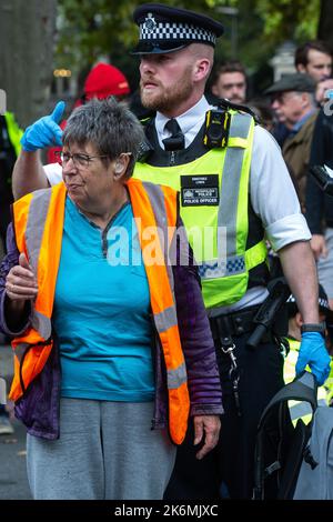 London, Großbritannien. 14.. Oktober 2022. Ein Beamter der Metropolitan Police verhaftete einen Klimaaktivisten von Just Stop Oil, der die Straße vor New Scotland Yard blockiert hatte, um die britische Regierung aufzufordern, die Erteilung von Öl- und Gaslizenzen einzustellen. Ein Aktivist besprühte auch das rotierende Schild von New Scotland Yard vor dem Gebäude mit gelber Farbe. Die Metropolitan Police nahm 24 Verhaftungen wegen des Verdachts der vorsätzlichen Behinderung der Autobahn und/oder der Verschwörung zur Begehung krimineller Schäden vor. Kredit: Mark Kerrison/Alamy Live Nachrichten Stockfoto
