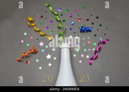 Konzept Für Das Neue Jahr 2023. Flache Champagner-Flasche auf grauer Fliese mit bunten Sternen und Band und dem Datum 2023 Stockfoto