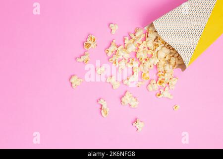 Snack-Konzept, süßes Popcorn aus der Papiertasse auf rosa Hintergrund ausgegossen. Stockfoto