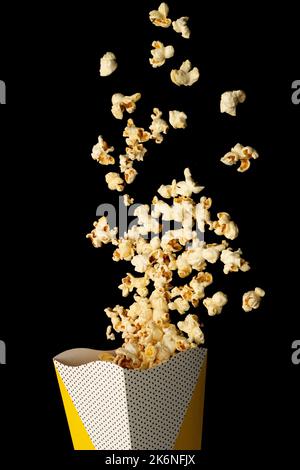 Snack-Konzept, süßes Popcorn, das aus dem Papierbecher auf pinkem Hintergrund schwimmt. Stockfoto