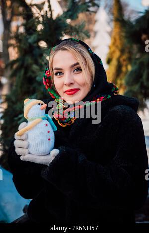 Schöne junge Frau in einem nationalen ukrainischen Kopftuch hält einen Schneemann Stockfoto