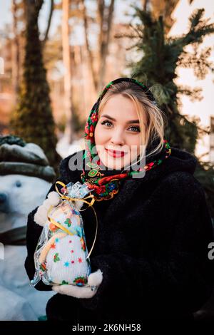 Schöne junge Frau in einem nationalen ukrainischen Kopftuch hält einen Schneemann Stockfoto