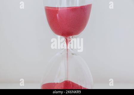 Roter Sand, der durch die Glühbirnen einer Sanduhr läuft, die Zeit zählt, kein Zeitkonzept Stockfoto