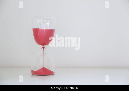 Eine Sanduhr links von weißem Hintergrund isoliert, roter Sand rutscht weg, Messung des Zeitverlaufes, läuft aus der Zeit Konzept Stockfoto