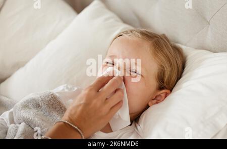 Sie werden sich bald besser fühlen. Eine Mutter wischte ihre kleinen Mädchen Nase mit einem Gewebe im Bett zu Hause von einem kleinen Mädchen krank im Bett zu Hause fühlen und bläst sie Stockfoto