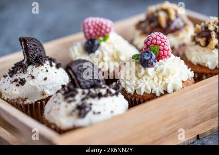 Leckere süße Muffins mit Mascarpone-Creme und Schokolade, Himbeere und Heidelbeere. Frisch gebackene Süßigkeiten mit Obst. In Holzkiste platziert. Stockfoto