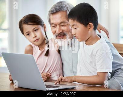 Eine Familie zu sein bedeutet, dass Sie ein Teil von etwas sind. Ein Großvater hilft seinen Enkeln bei ihren Hausaufgaben zu Hause. Stockfoto