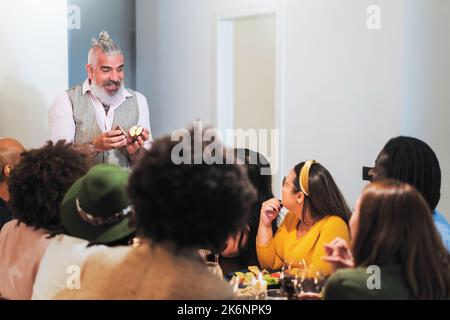 Hipster bärtiger Mann mit Apfel im Gespräch mit Freunden, die in der Küche essen - multiethnische Freunde, die zusammen essen und trinken - die Menschen am lebtesten Stockfoto