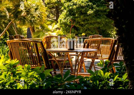 Blick auf einen leeren Sitzbereich mit Bambusmöbeln in einem idyllischen Garten unter Palmen mit tropischen Bambusstühlen und einem Tisch mit saftigem Essen. Stockfoto