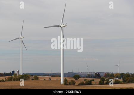 Windturbinen sind an bewölkten Tagen in einem ländlichen Gebiet zu sehen; Farmen und Silos sind im Hintergrund zu sehen. Stockfoto