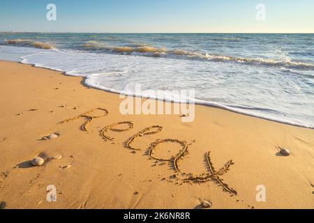 Wort entspannen handgeschrieben am Sandstrand bei Sonnenuntergang. Natur und konzeptuelle Szene. Stockfoto