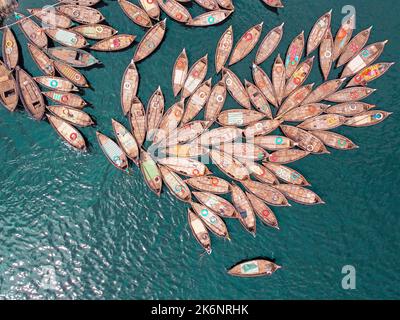 Hunderte von Holzbooten ziehen sich in Mustern um ihre Anlegestellen herum, die wie Blütenblätter aussehen, um am Morgen auf dem Fluss Buriganga zu pendeln. Stockfoto