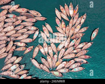 Hunderte von Holzbooten ziehen sich in Mustern um ihre Anlegestellen herum, die wie Blütenblätter aussehen, um am Morgen auf dem Fluss Buriganga zu pendeln. Stockfoto