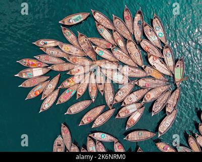 Hunderte von Holzbooten ziehen sich in Mustern um ihre Anlegestellen herum, die wie Blütenblätter aussehen, um am Morgen auf dem Fluss Buriganga zu pendeln. Stockfoto