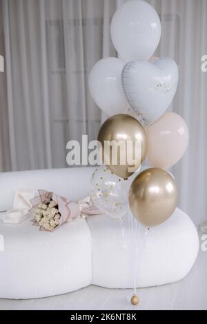 Dekoriertes Zimmer zu Hause für eine Überraschungsparty. Blumenstrauß und Banno-Kuchen auf dem Sofa. Ein paar bunte Luftballons.Glücklichen Geburtstag für achtzehn-jährige Mädchen Stockfoto