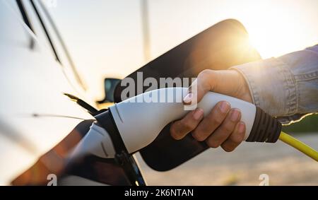 Frau lädt ein Elektroauto an der elektrischen Tankstelle mit Sonnenlicht Stockfoto