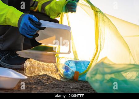 Ein ehrenamtlicher Mann sammelt bei Sonnenuntergang Plastikmüll im Park. Konzept der Reinigungsumgebung Stockfoto