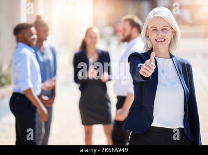 Du bist auf dem richtigen Weg. Eine reife Geschäftsfrau, die draußen mit Daumen nach oben zeigt. Stockfoto