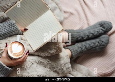 Gemütliches Zuhause, Frau mit warmer Decke bedeckt, trinkt Kaffee und reeds das Buch. Entspannen, sorglos, Komfort Lebensstil. Stockfoto