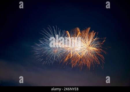 Nahaufnahme der Feuerwerksexplosion mit weißen und orangen Sternen. Isoliert am schwarzen und blauen Nachthimmel. Ideal für Sylvester und Neujahr. Stockfoto