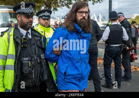 London, Großbritannien. 14.. Oktober 2022. Metropolitan Police Officers verhaften einen Klimaaktivisten von Just Stop Oil, der die Straße vor New Scotland Yard blockiert hatte, um die britische Regierung aufzufordern, die Erteilung von Öl- und Gaslizenzen einzustellen. Ein Aktivist besprühte auch das rotierende Schild von New Scotland Yard vor dem Gebäude mit gelber Farbe. Die Metropolitan Police nahm 24 Verhaftungen wegen des Verdachts der vorsätzlichen Behinderung der Autobahn und/oder der Verschwörung zur Begehung krimineller Schäden vor. Kredit: Mark Kerrison/Alamy Live Nachrichten Stockfoto