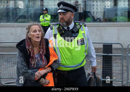 London, Großbritannien. 14.. Oktober 2022. Ein Beamter der Metropolitan Police verhaftete einen Klimaaktivisten von Just Stop Oil, der die Straße vor New Scotland Yard blockiert hatte, um die britische Regierung aufzufordern, die Erteilung von Öl- und Gaslizenzen einzustellen. Ein Aktivist besprühte auch das rotierende Schild von New Scotland Yard vor dem Gebäude mit gelber Farbe. Die Metropolitan Police nahm 24 Verhaftungen wegen des Verdachts der vorsätzlichen Behinderung der Autobahn und/oder der Verschwörung zur Begehung krimineller Schäden vor. Kredit: Mark Kerrison/Alamy Live Nachrichten Stockfoto