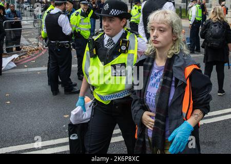 London, Großbritannien. 14.. Oktober 2022. Ein Beamter der Metropolitan Police verhaftete einen Klimaaktivisten von Just Stop Oil, der die Straße vor New Scotland Yard blockiert hatte, um die britische Regierung aufzufordern, die Erteilung von Öl- und Gaslizenzen einzustellen. Ein Aktivist besprühte auch das rotierende Schild von New Scotland Yard vor dem Gebäude mit gelber Farbe. Die Metropolitan Police nahm 24 Verhaftungen wegen des Verdachts der vorsätzlichen Behinderung der Autobahn und/oder der Verschwörung zur Begehung krimineller Schäden vor. Kredit: Mark Kerrison/Alamy Live Nachrichten Stockfoto