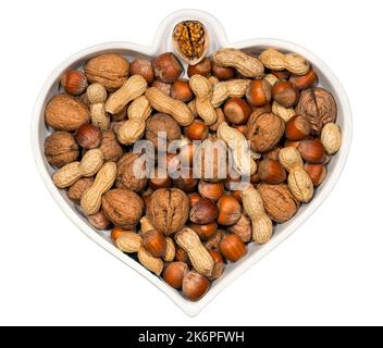 Weiße herzförmige Schale mit getrockneten Früchten (Erdnüsse, Walnüsse, Haselnüsse), isoliert auf weißem Hintergrund. Stockfoto