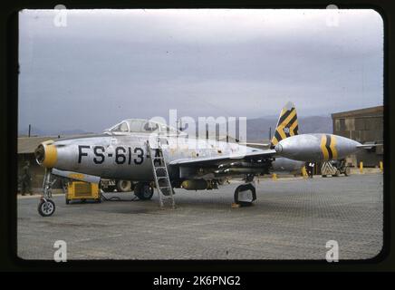 Eine halbe linke Vorderansicht einer Republic F-84E Thunder 'Lois K' (s/n 51-613) der 8. Fighter Bomber Squadron (FBS), 49. Fighter Bomber Group (FBG), ausgestattet mit externen Kraftstofftanks, einer Bombe und vier Raketen, irgendwo in Korea. Die drei Tip-Tank-Streifen identifizieren den Piloten dieses Flugzeugs als Staffelführer. Eine Leiter wird an der Seite des Flugzeugs abgestellt, die zum Cockpit führt. Im Hintergrund ist ein Bodenbemann zu sehen, ebenso wie einige Gebäude und Geräte. Stockfoto