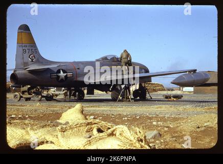 Eine halbe rechte Rückansicht eines Lockheed F-80C Shooting Star (s/n 49-755) mit den Markierungen des 41. Fighter Interceptor Squadron (FIS), 35. Fighter Interceptor Wing (FIW), irgendwo in Korea. Das Flugzeug steht vor Sandsäcken und einem Gebäude. Ein Besatzungsmacht steht auf dem rechten Flügel, und andere Arbeiten unter der Nase des Flugzeugs. Eine Leiter ragt vom Cockpit aus. Die Ausrüstung ist auf dem Boden rund um das Flugzeug verstreut. Auf der linken Seite des Flugzeugs sind ein Jeep und ein weiteres unterstützendes Fahrzeug zu sehen. Stockfoto