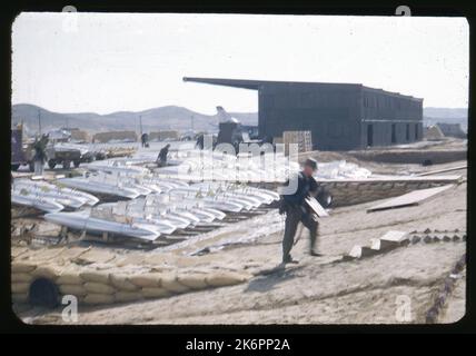 Ein Flugplatz irgendwo in Korea, mit Reihen von externen Kraftstofftanks. Im Hintergrund ist ein nordamerikanischer Säbel F-86 zu sehen. Ein weiteres Flugzeug ist sichtbar, geparkt in einem Nasenhangar. Stockfoto