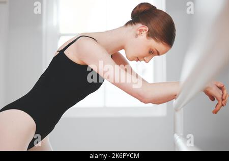 Nutze deine Emotionen und drücke sie in deinen Bewegungen aus. Eine junge Balletttänzerin, die sich an einer Barre lehnt. Stockfoto