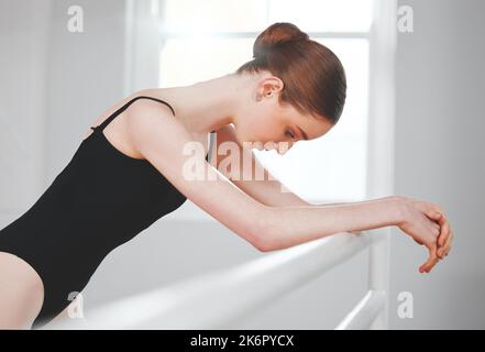 Ich hoffe, dass ich das richtig verstehe. Eine junge Balletttänzerin, die sich an einer Barre lehnt. Stockfoto