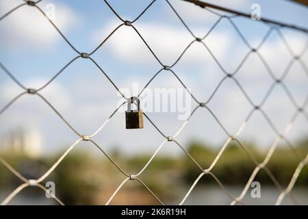 Altes rostiger Verschluss, der an einem Draht auf einer Brücke befestigt ist Stockfoto