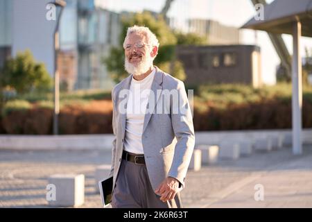 Fröhlicher, stilvoller alter, professioneller Geschäftsmann, der in der Großstadt draußen unterwegs ist. Stockfoto