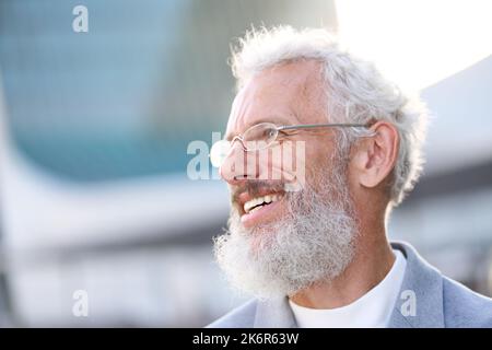 Lächelnder, glücklicher, älterer Geschäftsmann, der im Freien einen Anzug trägt, ein Kopfbildnis. Stockfoto