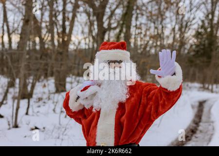 Sehen Sie den Weihnachtsmann, der in der Nähe des Waldes läuft, mit roten Tüten gefüllt mit Geschenken für Kinder zu Weihnachten, umgeben von weißem Schnee Stockfoto