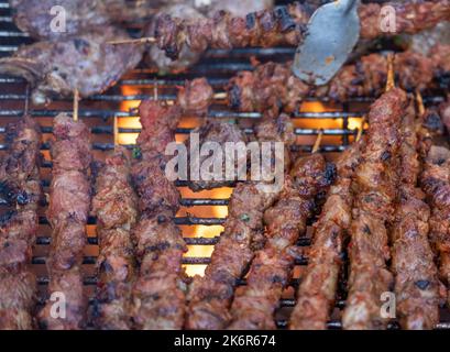 Heißes gegrilltes Lammfleisch auf Spießen und Fleischbällchen, die während einer Grillparty am offenen Kamin gegrillt wurden Stockfoto