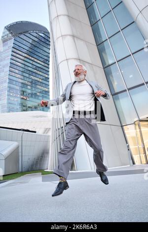 Glücklicher älterer, professioneller Geschäftsmann, der in der Großstadt im Freien springt. Stockfoto