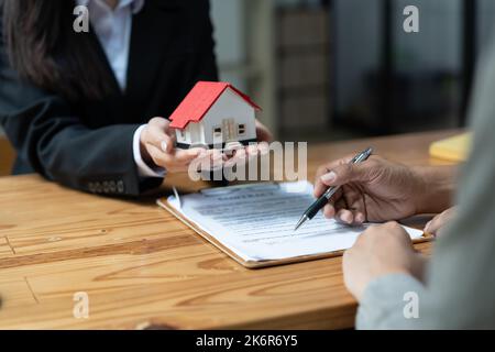 Immobilienmakler mit Kunden, die einen Deal abschließen und einen Vertrag unterzeichnen. Stockfoto