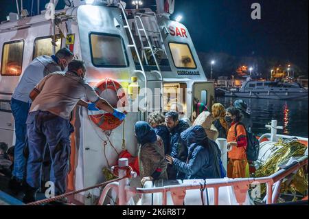 Roccella Jonica, Italien. 14. Oktober 2022. Mitglieder der Küstenwache unterstützen Migranten beim Aussteigen aus dem Boot. Patrouillenboote der italienischen Küstenwache befahren zwei verschiedene Gruppen von Migranten (99 Personen in der ersten, 83 in der zweiten, beide von der türkischen Route) im Hafen „Porto delle Grazie“ von Roccella Jonica. Die große Mehrheit der Migranten stammt aus dem Iran, dem Irak, Afghanistan und Syrien, bei der zweiten Ankunft kommen Menschen aus Bangladesch. Ärzte ohne Grenzen und das lokale Komitee des Roten Kreuzes unterstützten Migranten im Hafen. Kredit: SOPA Images Limited/Alamy Live Nachrichten Stockfoto