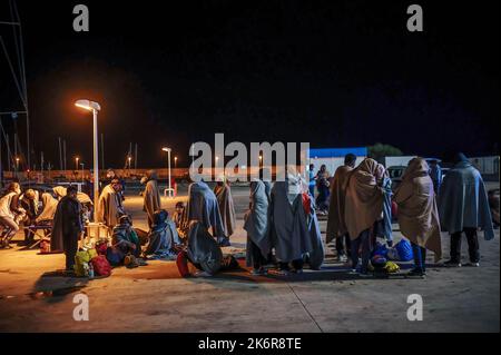 Roccella Jonica, Italien. 14. Oktober 2022. Migranten sahen, wie sie warteten, bis sie zur erste-Hilfe-Stelle gehen konnten. Patrouillenboote der italienischen Küstenwache befahren zwei verschiedene Gruppen von Migranten (99 Personen in der ersten, 83 in der zweiten, beide von der türkischen Route) im Hafen „Porto delle Grazie“ von Roccella Jonica. Die große Mehrheit der Migranten stammt aus dem Iran, dem Irak, Afghanistan und Syrien, bei der zweiten Ankunft kommen Menschen aus Bangladesch. Ärzte ohne Grenzen und das lokale Komitee des Roten Kreuzes unterstützten Migranten im Hafen. Kredit: SOPA Images Limited/Alamy Live Nachrichten Stockfoto