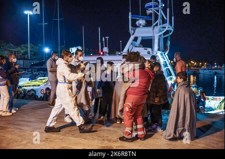Roccella Jonica, Italien. 14. Oktober 2022. Mitglieder des Roten Kreuzes unterstützen Migranten beim Aussteigen aus dem Boot. Patrouillenboote der italienischen Küstenwache befahren zwei verschiedene Gruppen von Migranten (99 Personen in der ersten, 83 in der zweiten, beide von der türkischen Route) im Hafen „Porto delle Grazie“ von Roccella Jonica. Die große Mehrheit der Migranten stammt aus dem Iran, dem Irak, Afghanistan und Syrien, bei der zweiten Ankunft kommen Menschen aus Bangladesch. Ärzte ohne Grenzen und das lokale Komitee des Roten Kreuzes unterstützten Migranten im Hafen. Kredit: SOPA Images Limited/Alamy Live Nachrichten Stockfoto