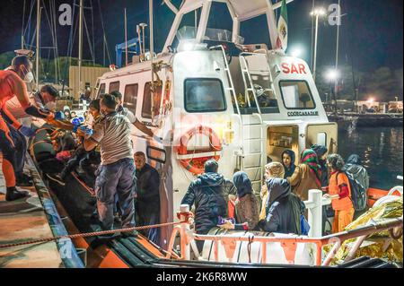 Roccella Jonica, Italien. 14. Oktober 2022. Mitglieder der Küstenwache während der Ausschiffung gesehen. Patrouillenboote der italienischen Küstenwache befahren zwei verschiedene Gruppen von Migranten (99 Personen in der ersten, 83 in der zweiten, beide von der türkischen Route) im Hafen „Porto delle Grazie“ von Roccella Jonica. Die große Mehrheit der Migranten stammt aus dem Iran, dem Irak, Afghanistan und Syrien, bei der zweiten Ankunft kommen Menschen aus Bangladesch. Ärzte ohne Grenzen und das lokale Komitee des Roten Kreuzes unterstützten Migranten im Hafen. Kredit: SOPA Images Limited/Alamy Live Nachrichten Stockfoto