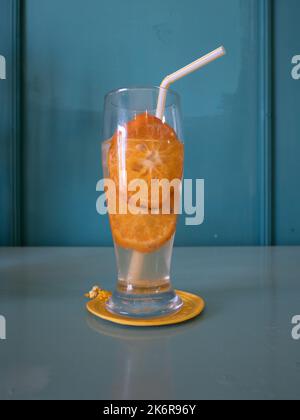 Glasbecher mit Ingwer-Kombucha mit Orangenscheiben auf einem Teal-Holztisch Stockfoto
