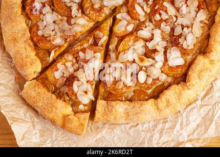 Nahaufnahme hausgemachter Kuchen mit Pflaumen und Mandelblättern auf Pergamentpapier. Draufsicht. Stockfoto