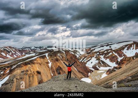 Fröhliche Wandererin, die am bewölkten Tag im isländischen Hochland von Landmannal auf dem vulkanischen Berg steht und vom Blahnjukur-Pfad schneebedeckt ist Stockfoto